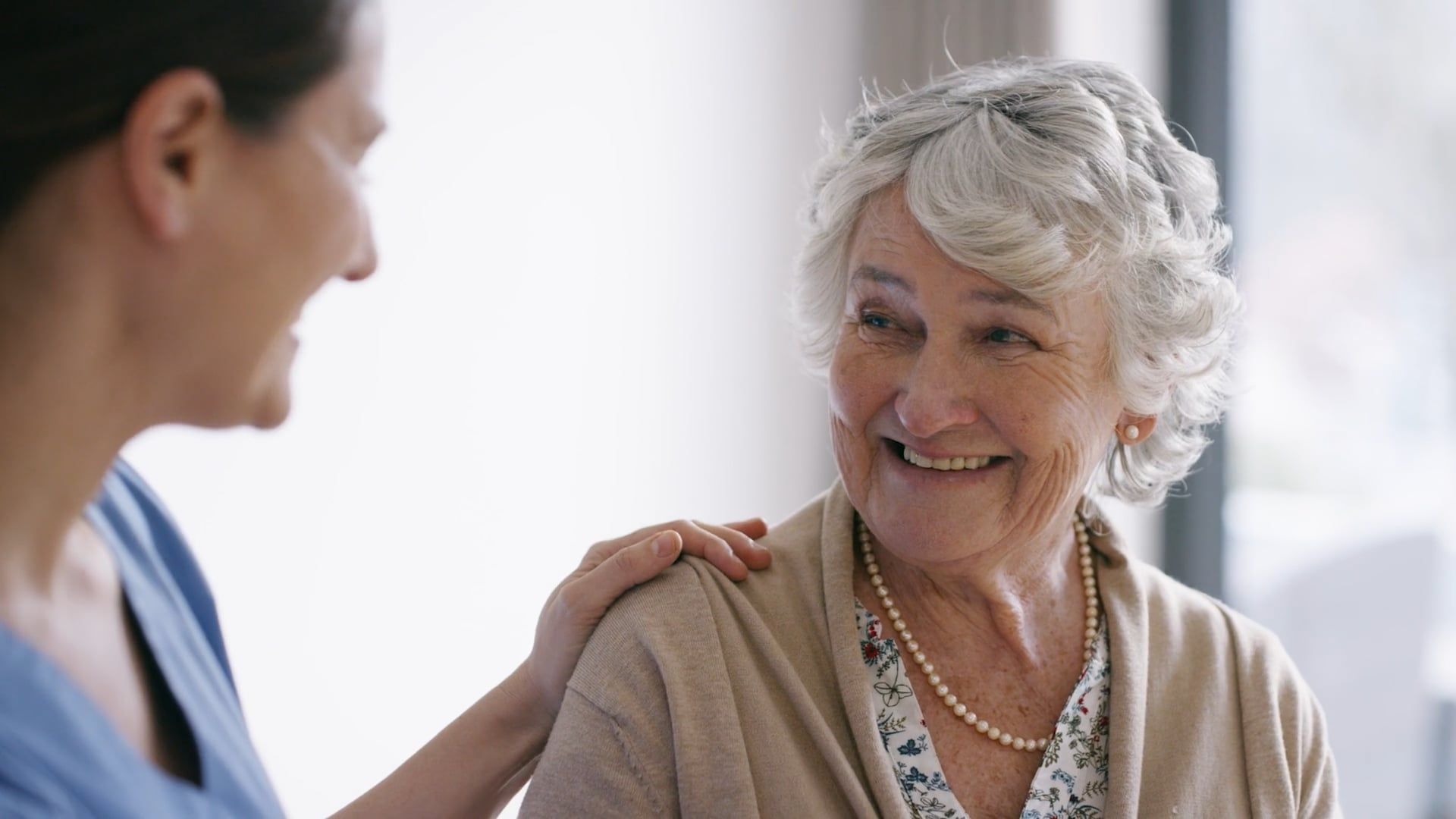 An elderly woman is smiling while talking to a nurse.