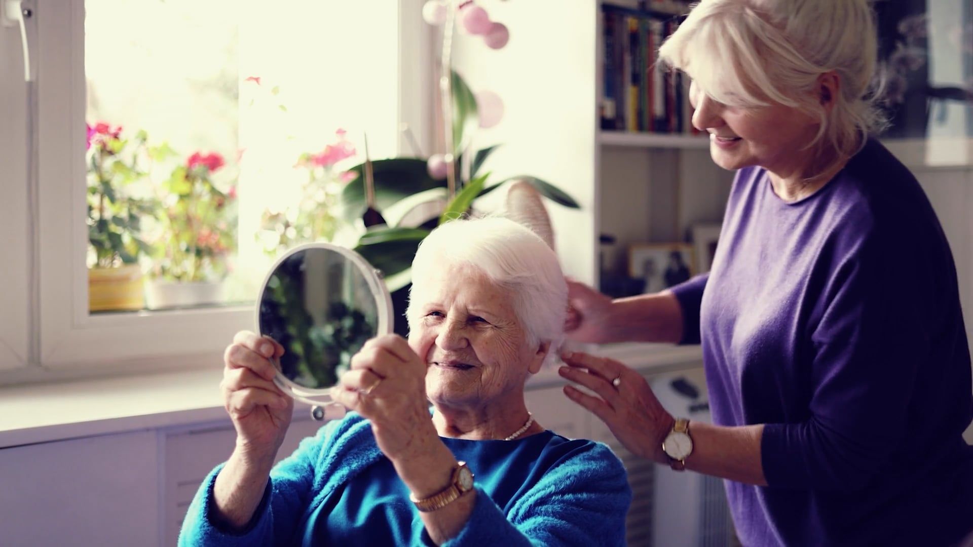 An elderly woman is looking at her hair in a mirror.
