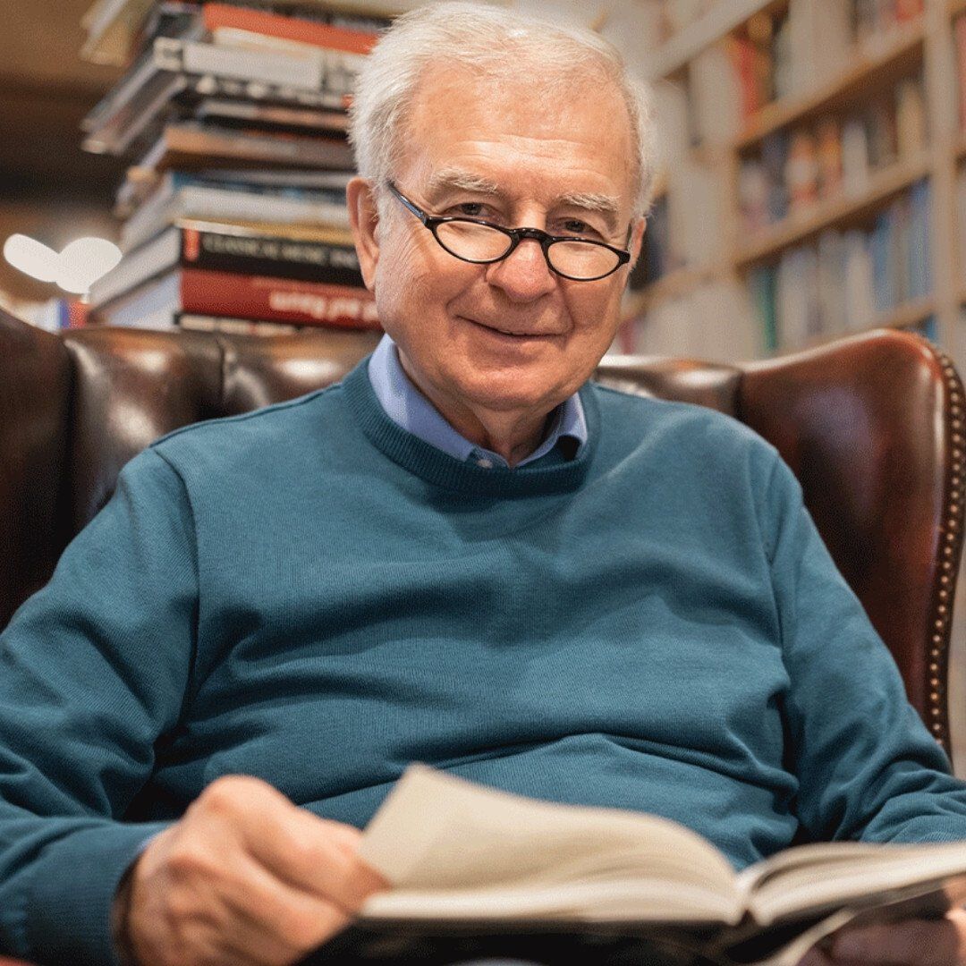 A man wearing glasses is sitting in a chair reading a book