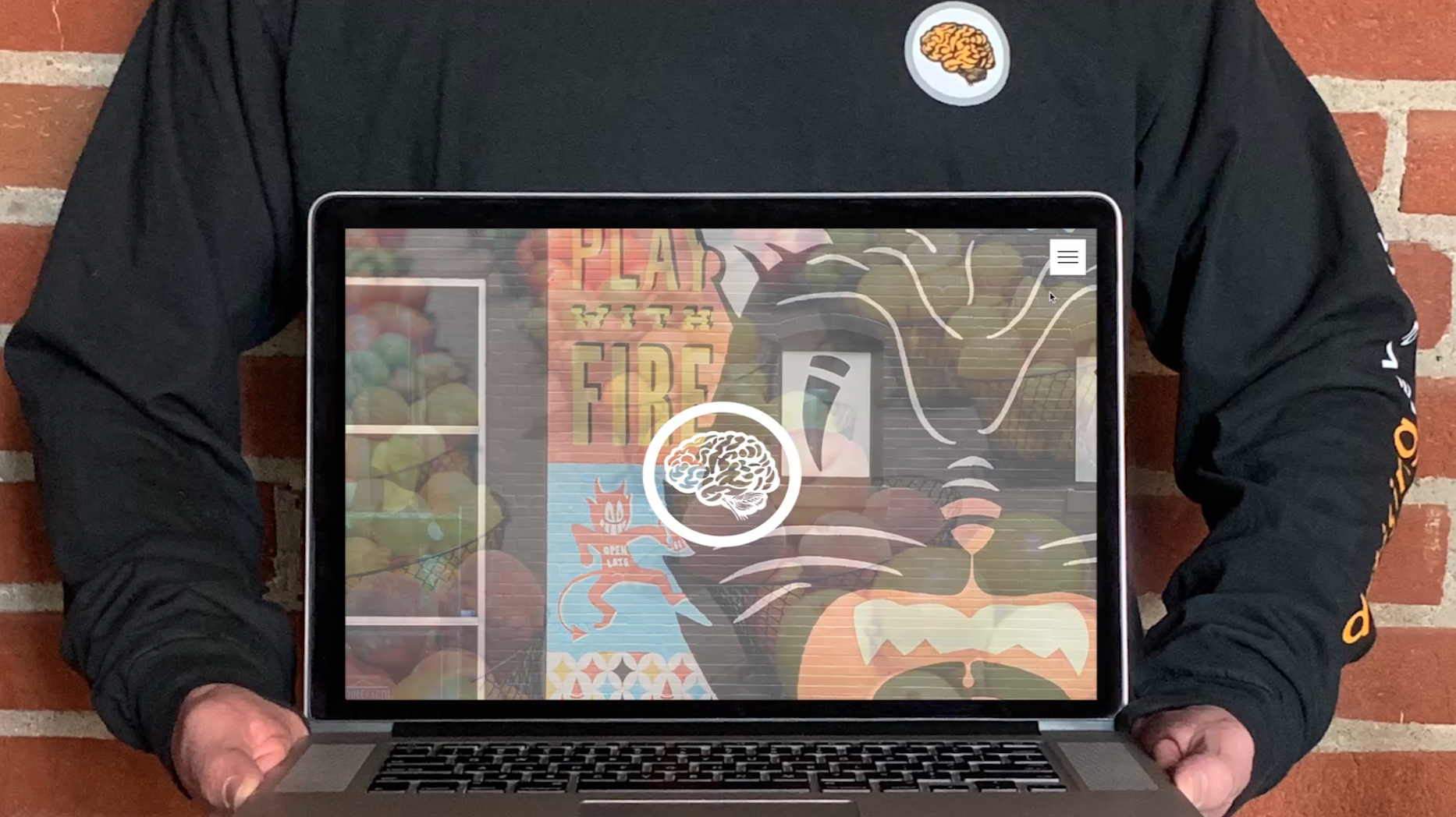 A person is holding a laptop computer in front of a brick wall.