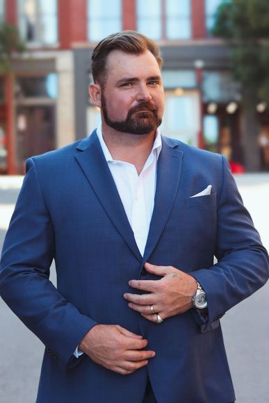 Man in blue suit adjusts jacket, urban background.