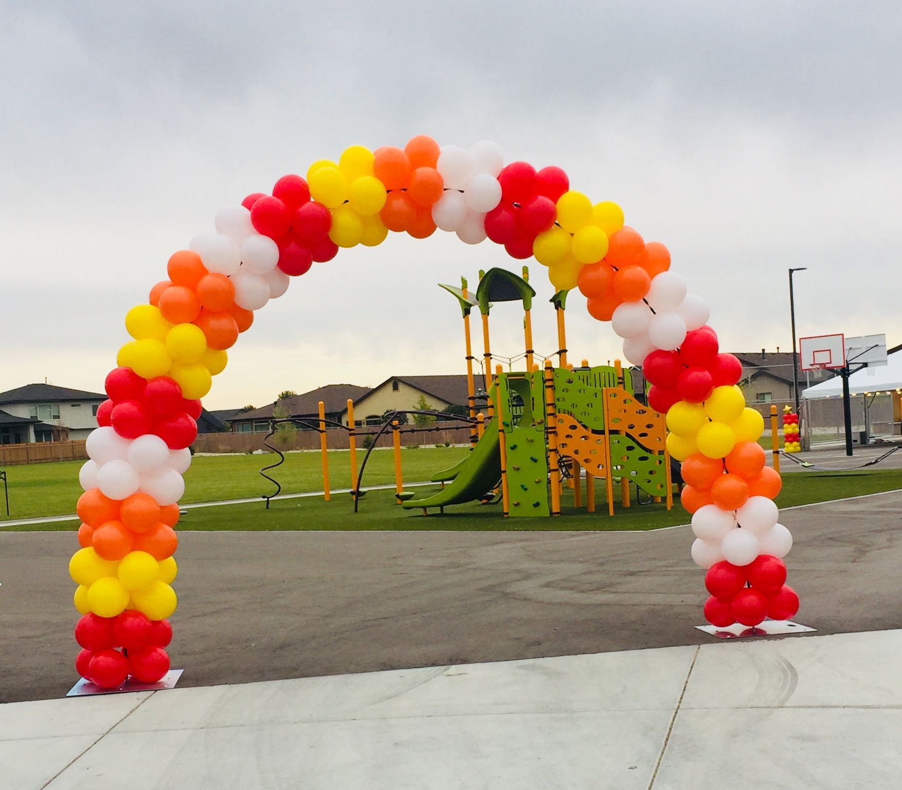 A red white and yellow balloon arch in front of a playground