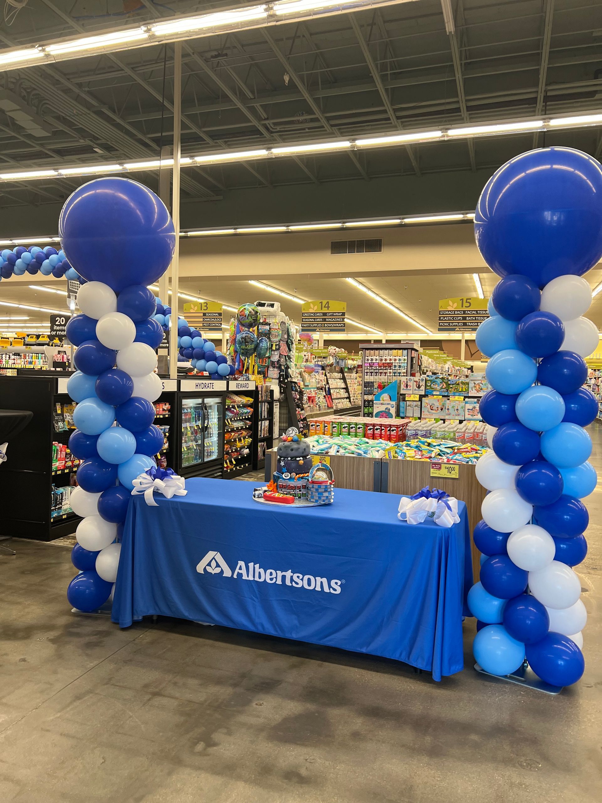 A table with a blue tablecloth is surrounded by blue and white balloons in a store.
