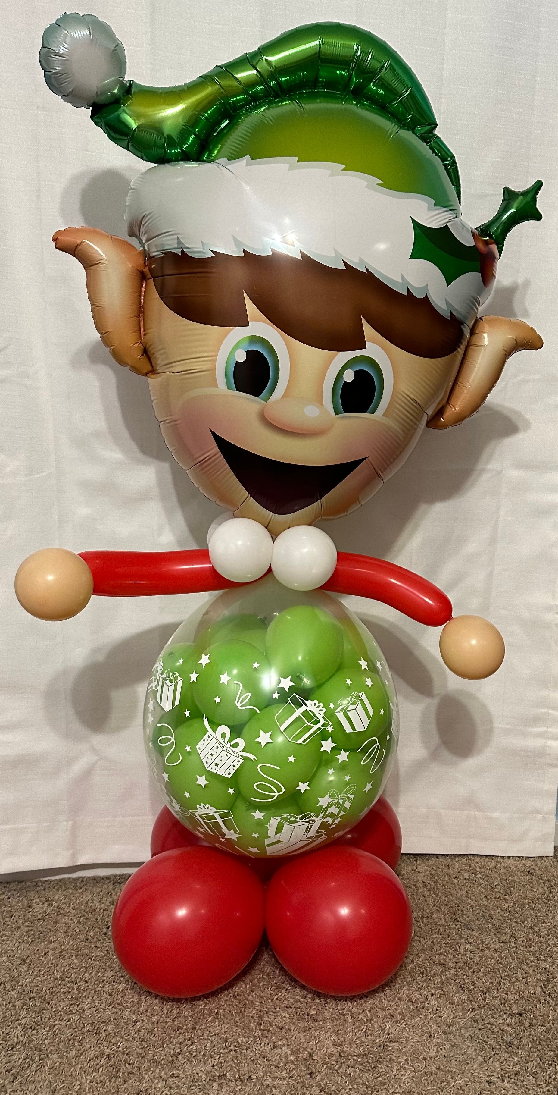 A balloon elf is standing next to a balloon filled with green balloons.