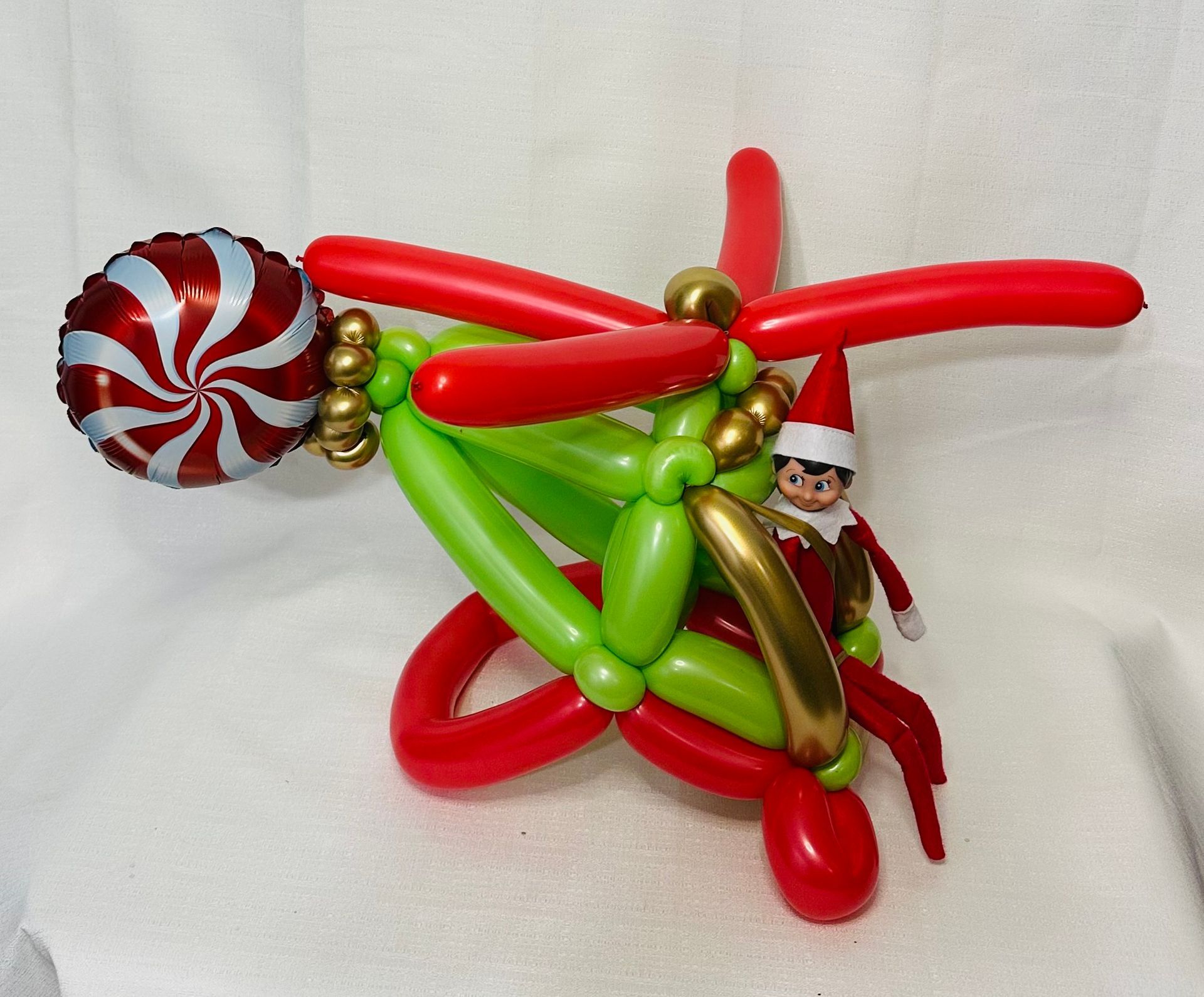 An elf on the shelf is riding a helicopter made of balloons