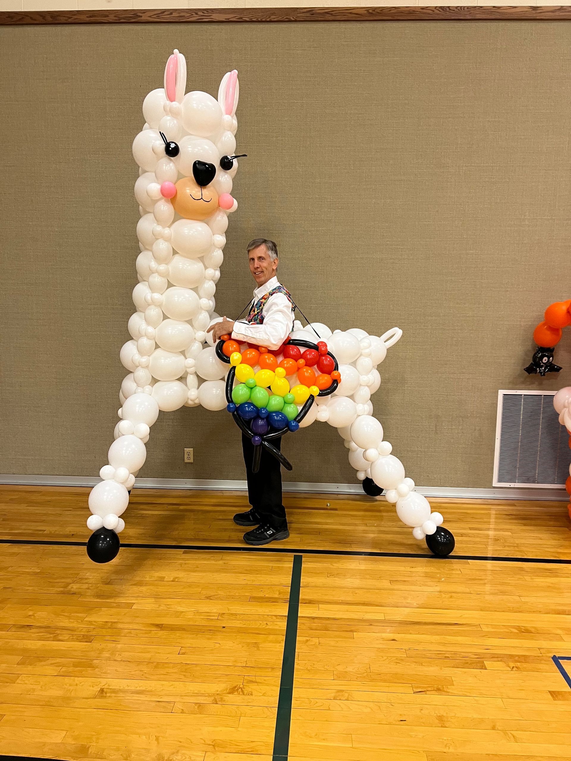 A man is standing next to a llama made out of balloons.