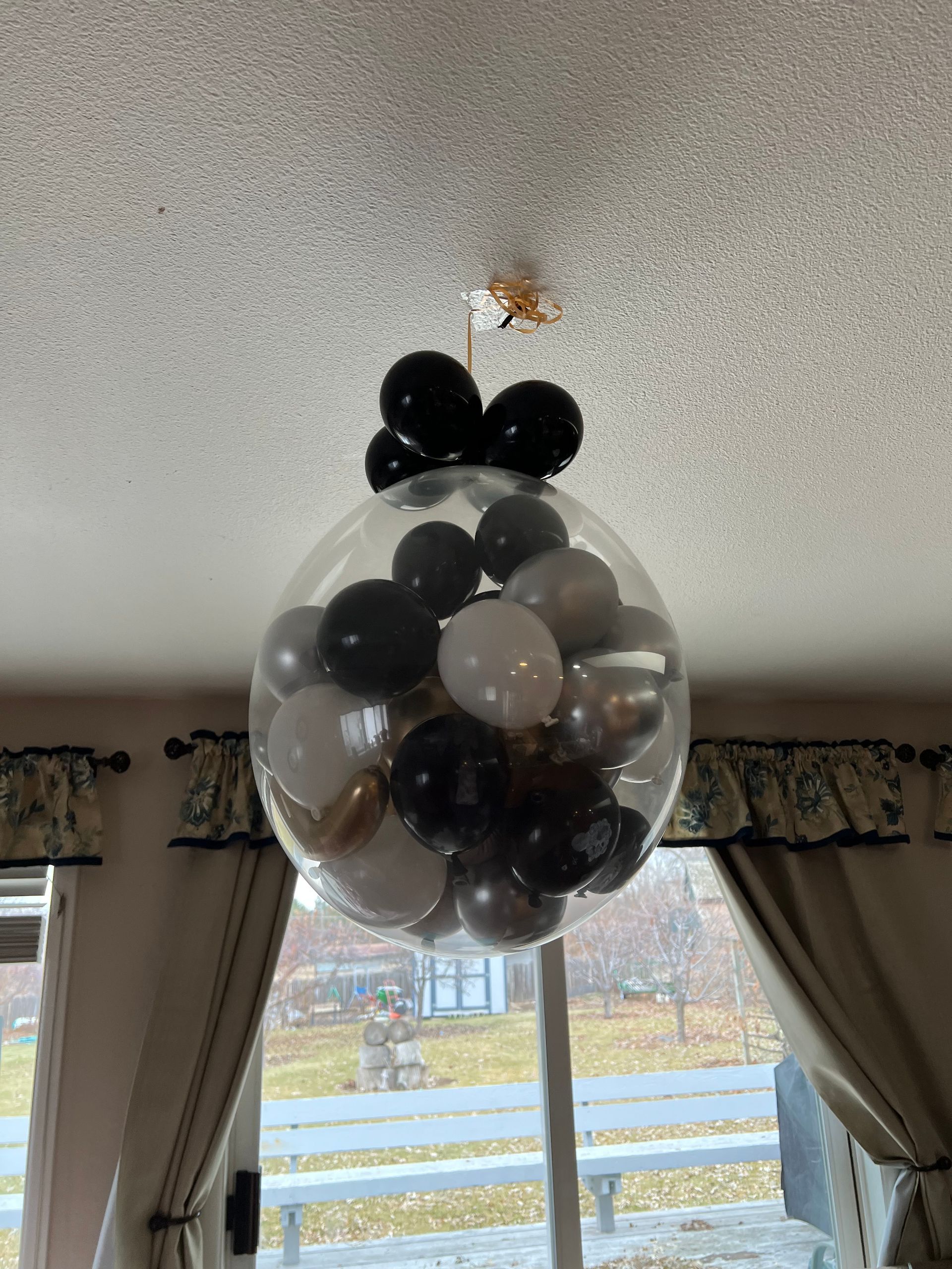 A clear balloon filled with black , white and gold balloons is hanging from the ceiling.