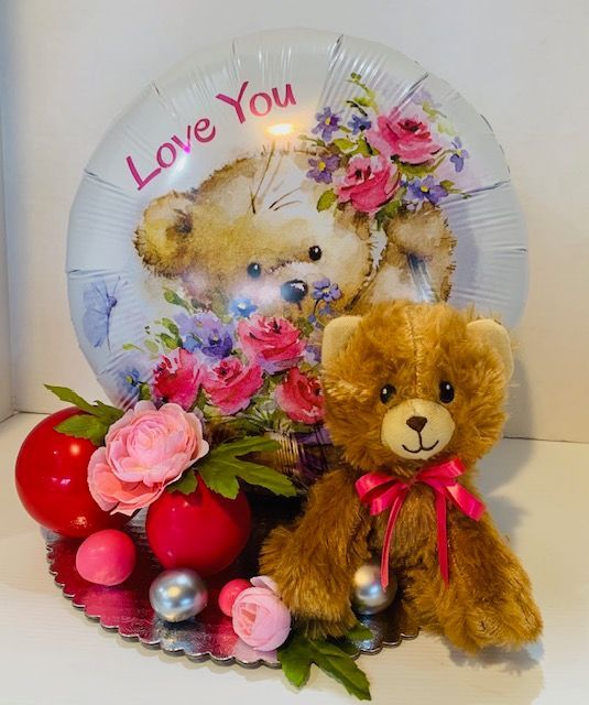 A teddy bear sits next to a love you balloon