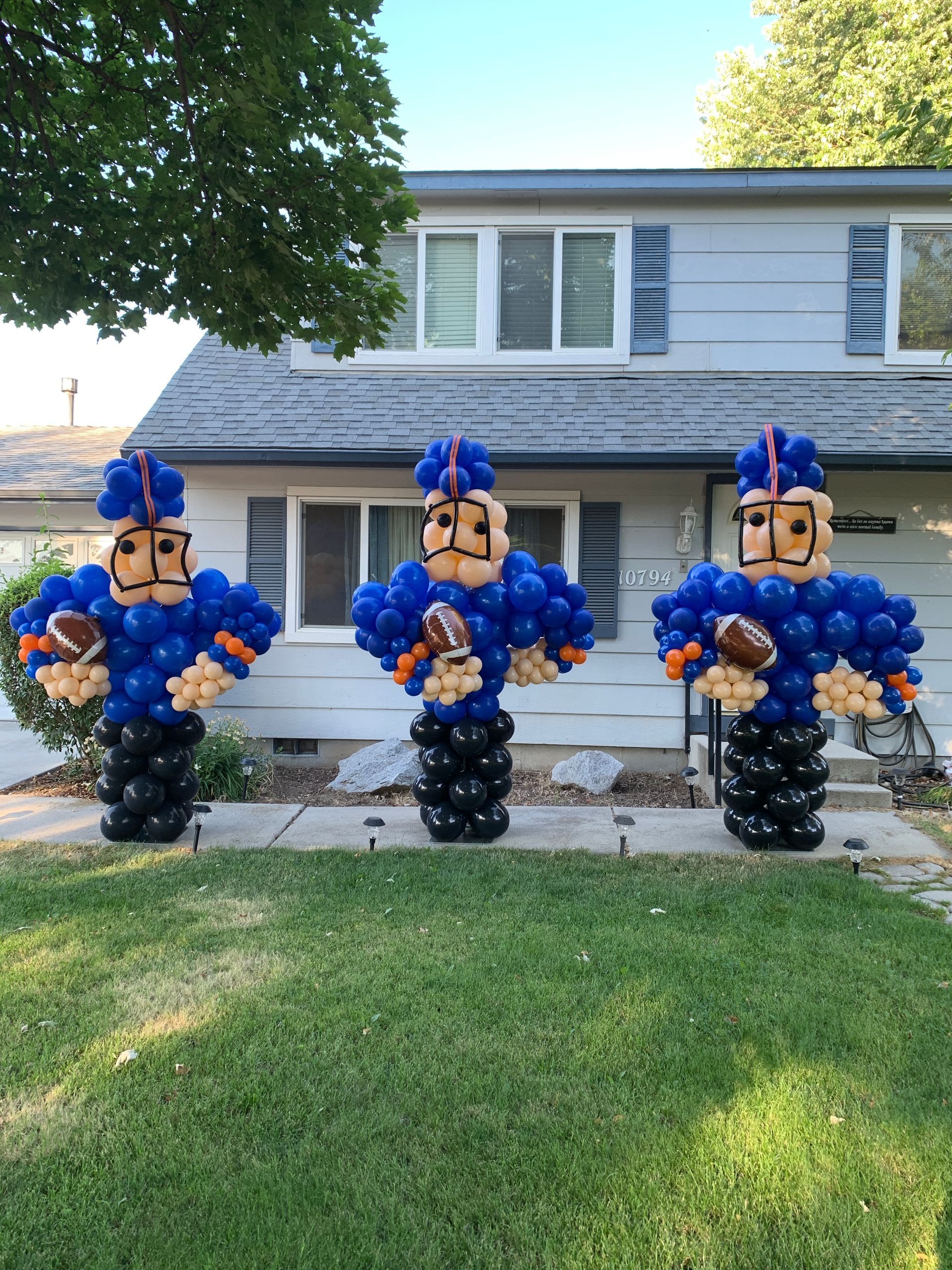 Three football players made out of balloons are standing in front of a house.