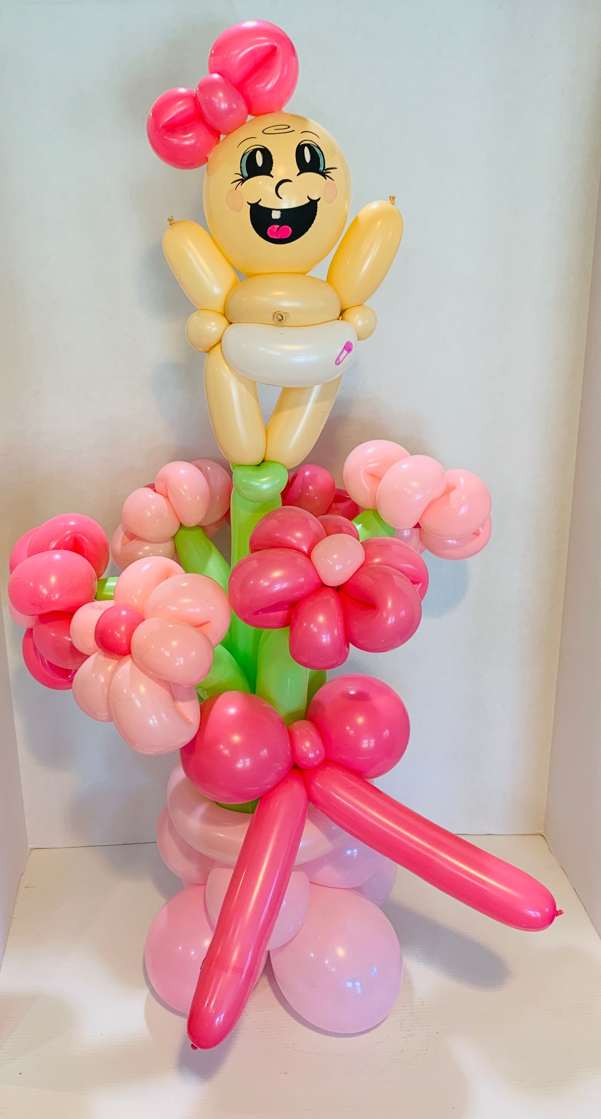 A baby made out of balloons is holding a bouquet of pink flowers.
