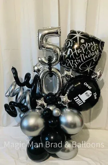 A bunch of black and silver balloons are sitting on a table.