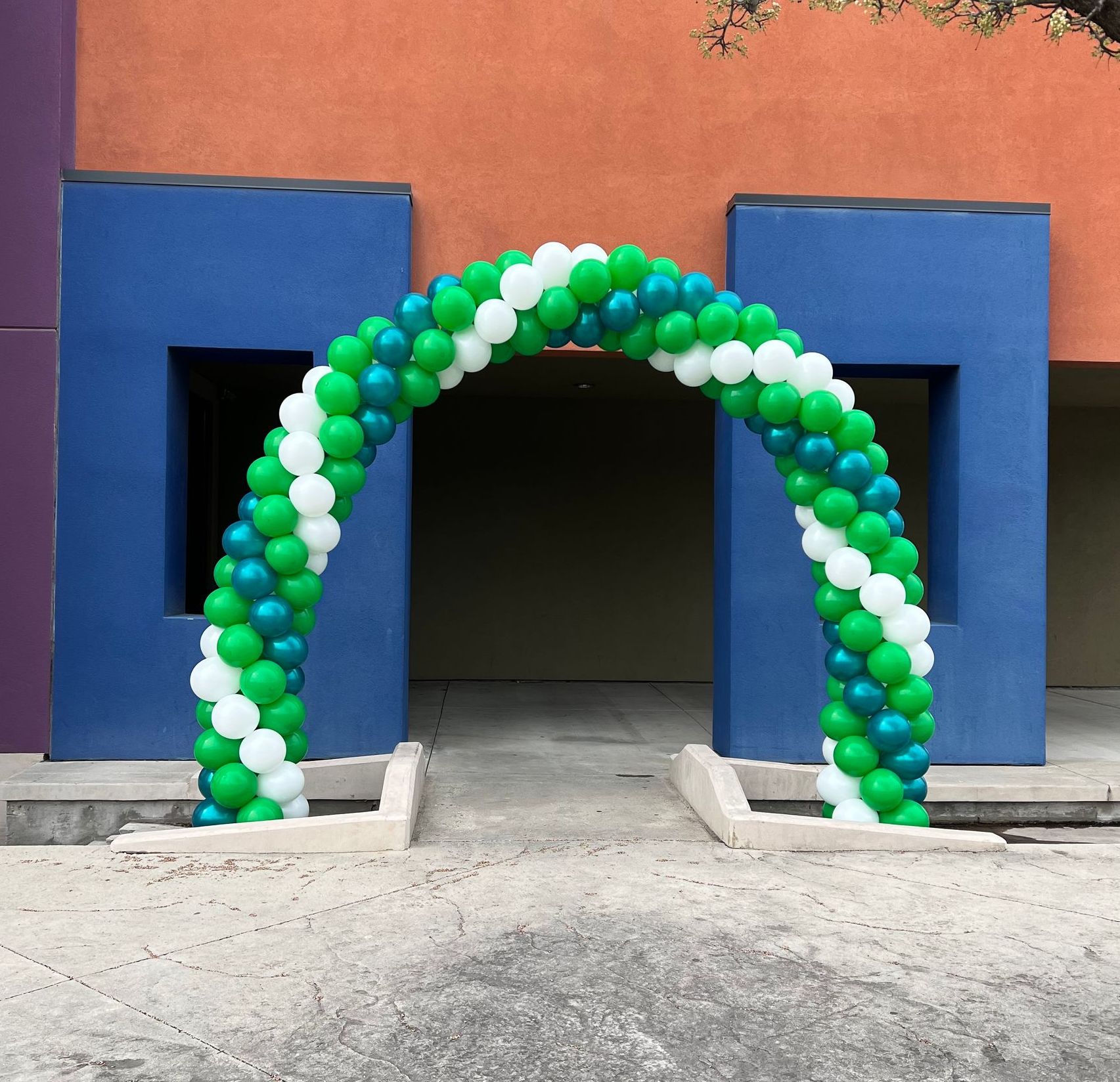 A green white and blue balloon arch in front of a building