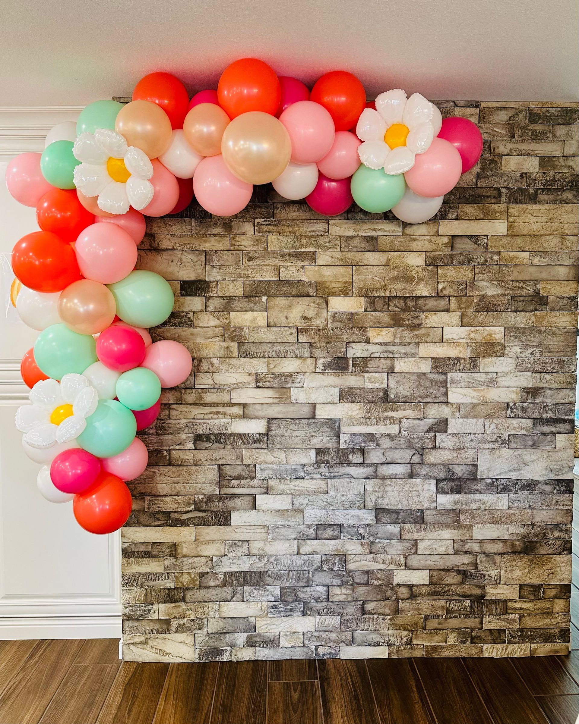A bunch of balloons are hanging on a brick wall.