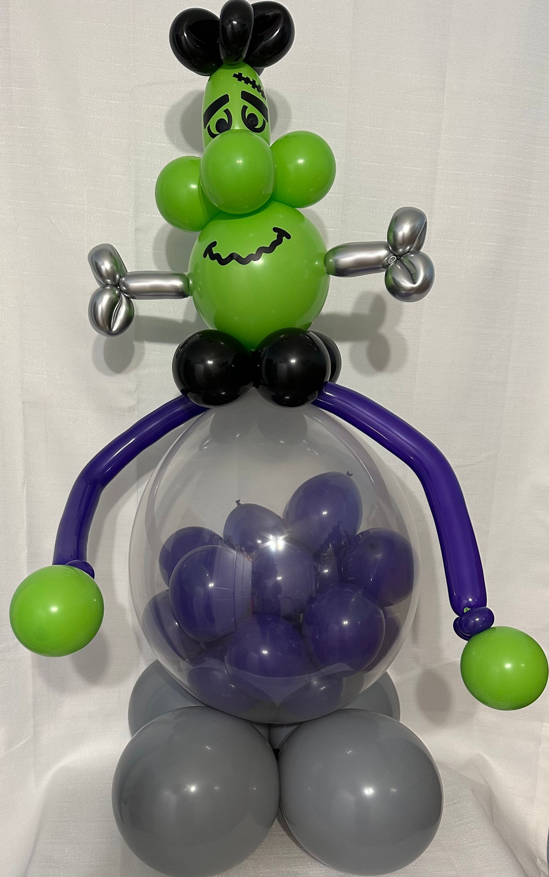 A green balloon monster is sitting on top of a balloon filled with purple balloons.