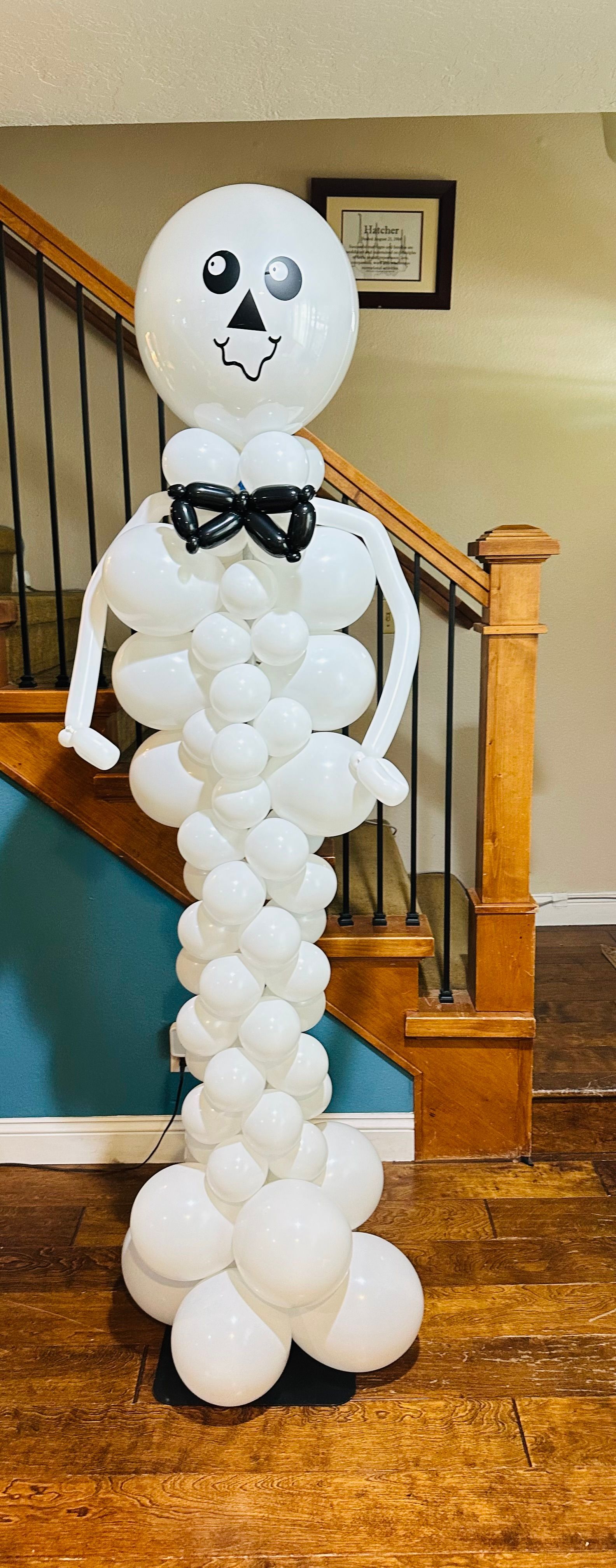 A skeleton made out of balloons is standing in front of a staircase.