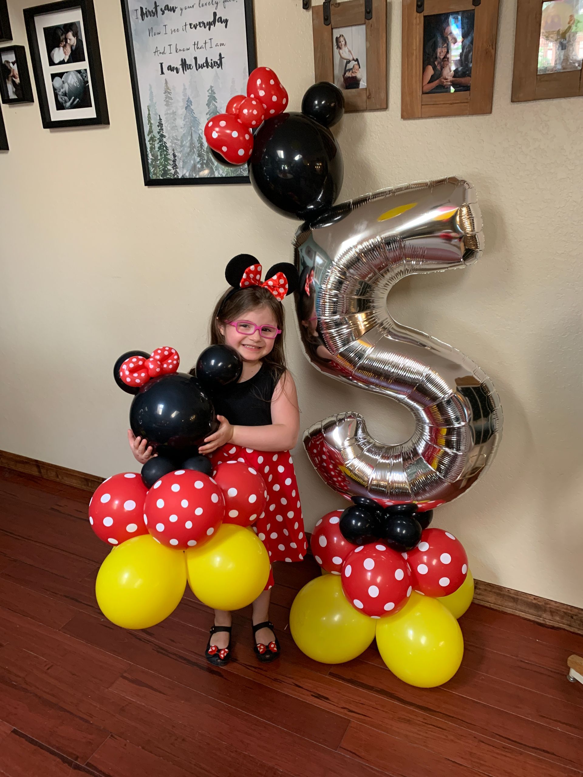 A little girl is holding a mickey mouse balloon and a number 5 balloon.