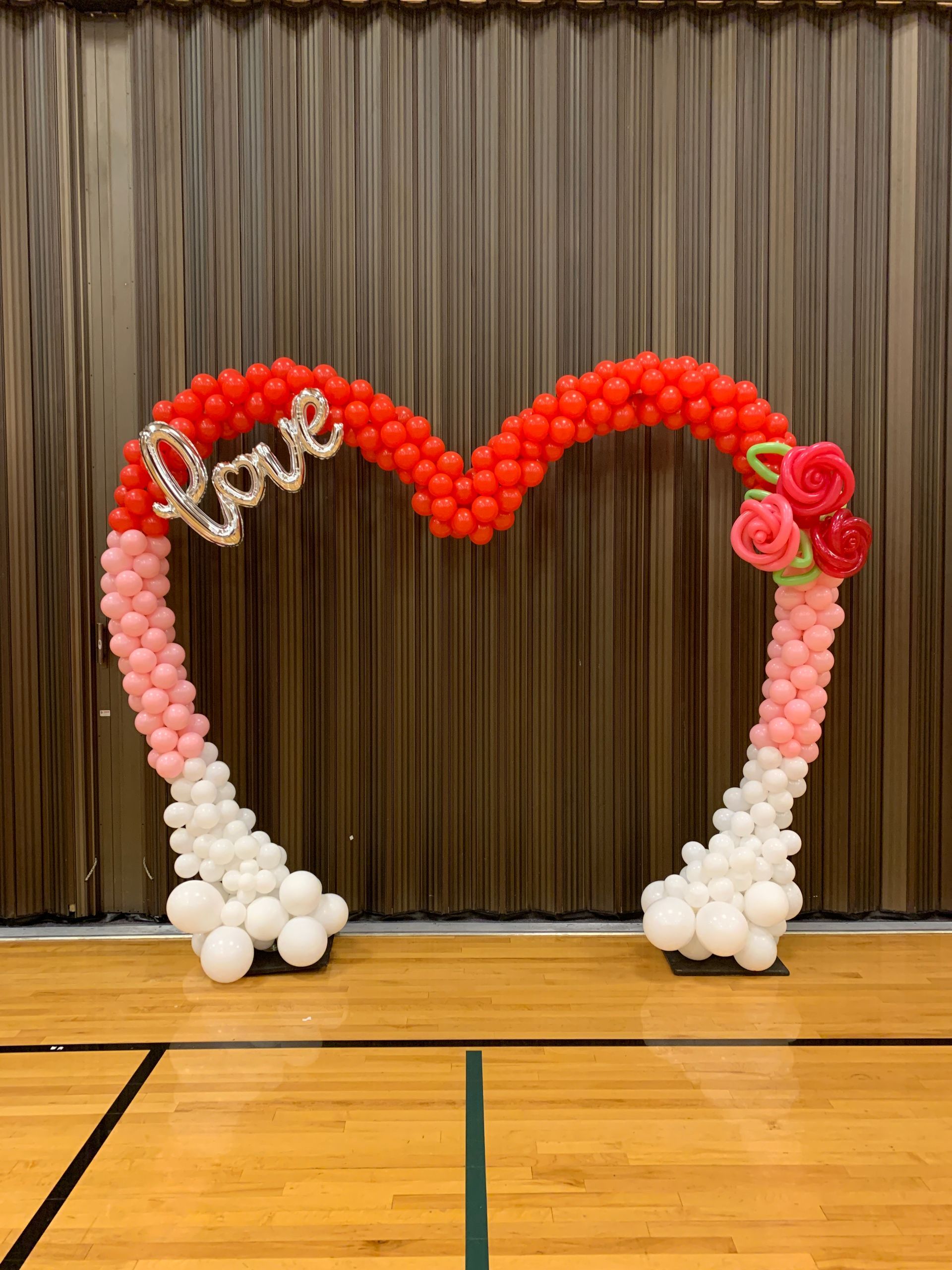 A heart shaped arch made of balloons in a gym.