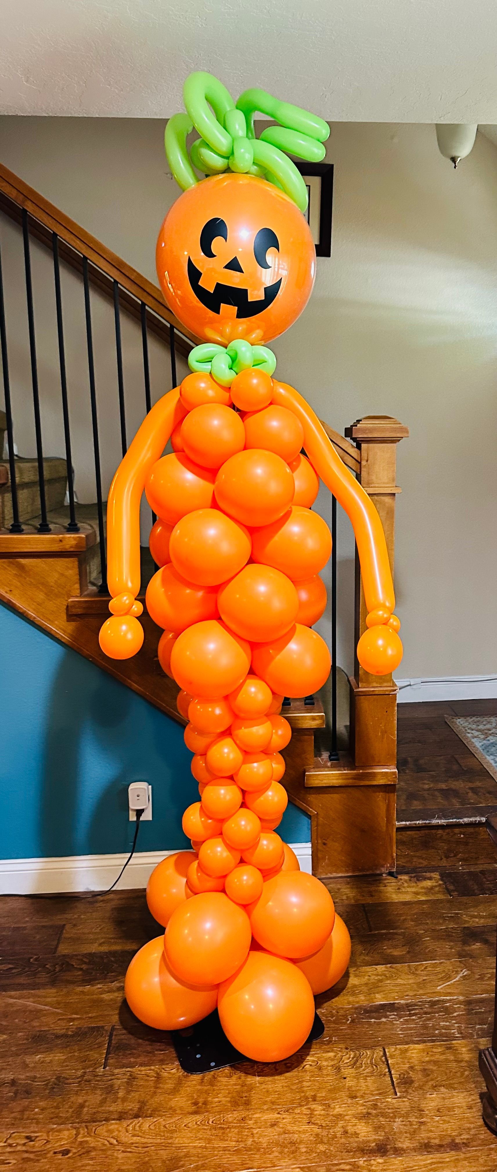 A pumpkin made out of balloons is standing in front of a staircase.