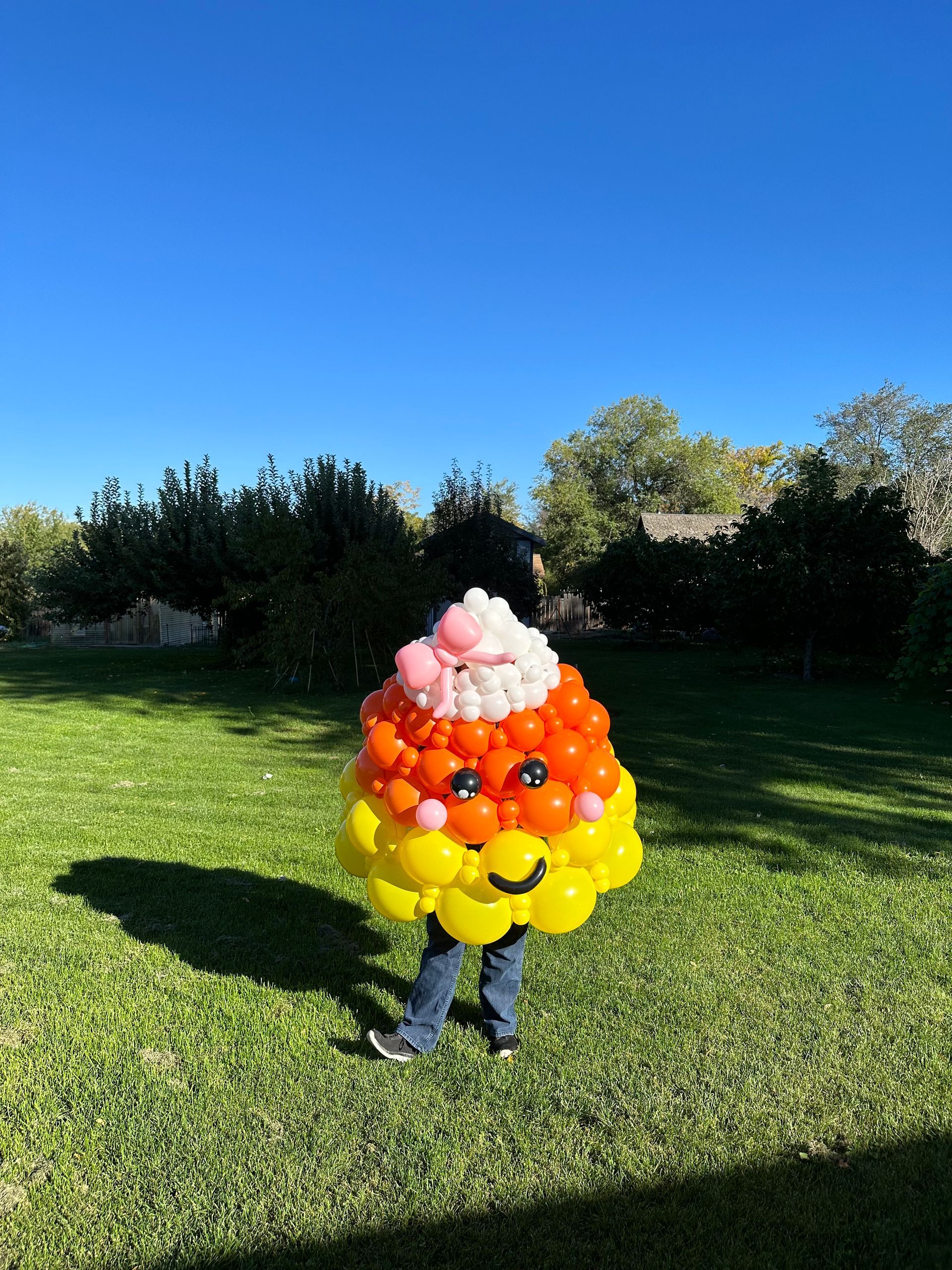 A person is wearing a candy corn costume made of balloons.