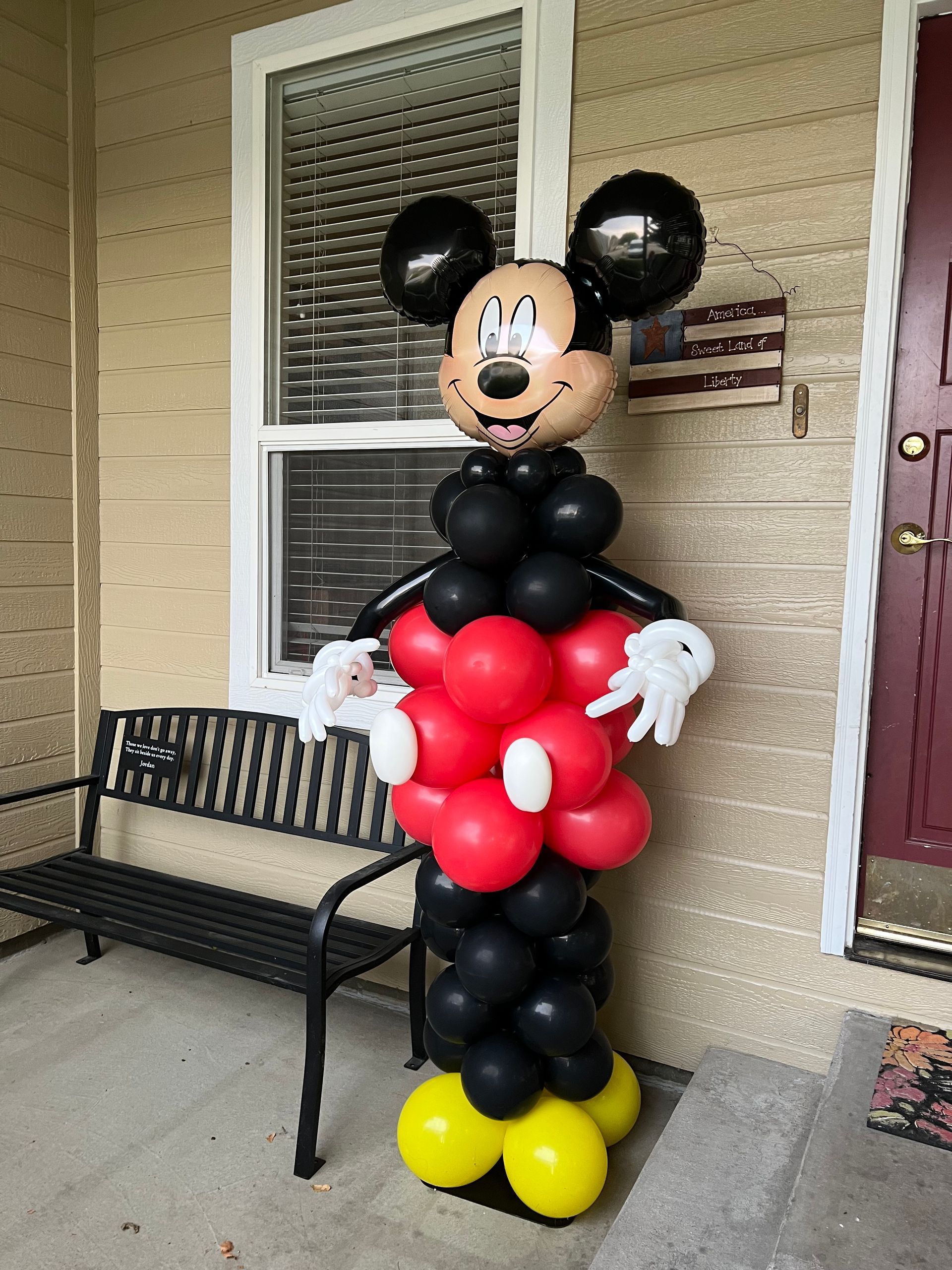A mickey mouse made of balloons is standing in front of a house.