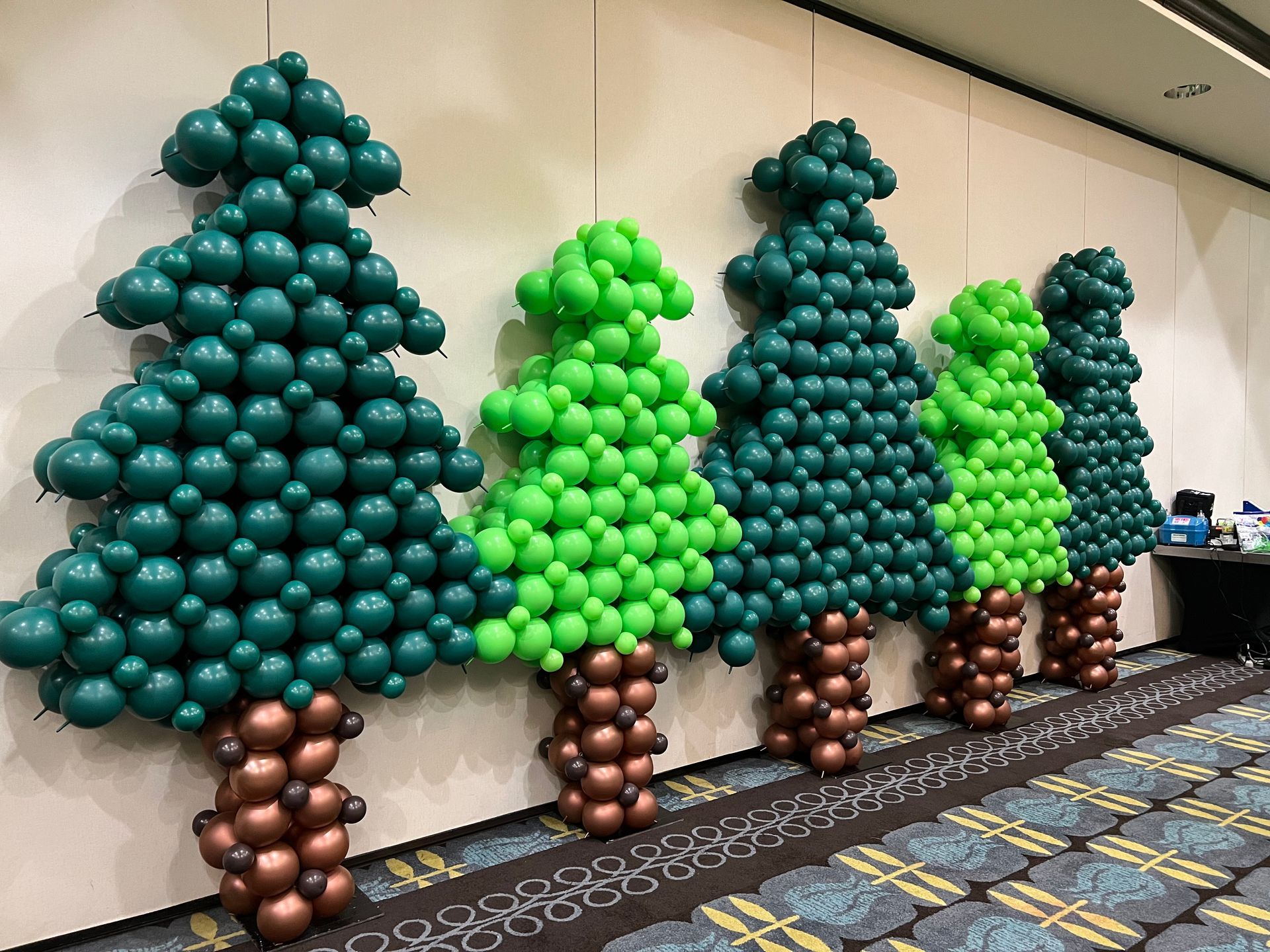 A row of balloons shaped like trees are lined up on a wall.