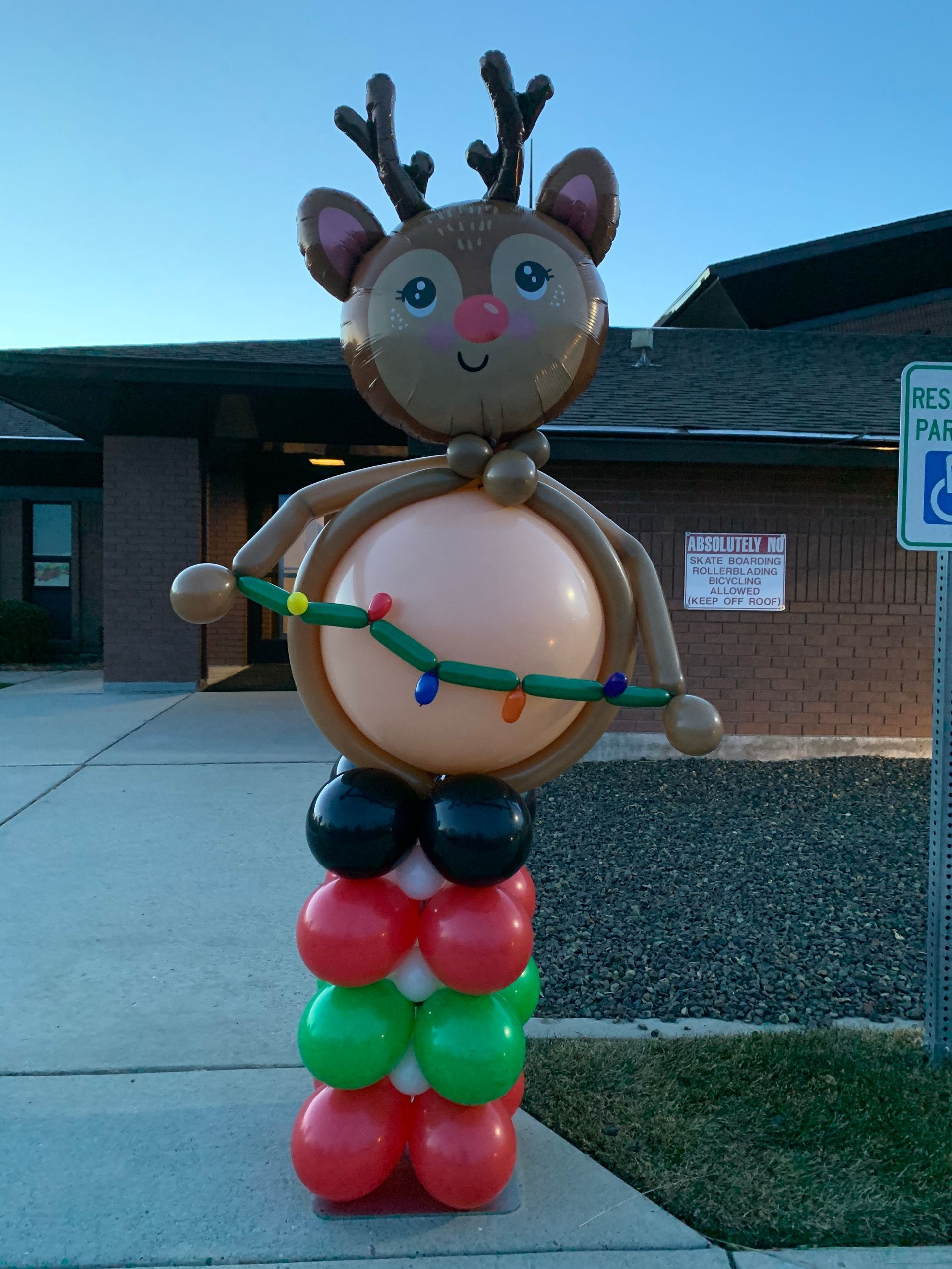 A reindeer made out of balloons is standing in front of a handicapped parking sign