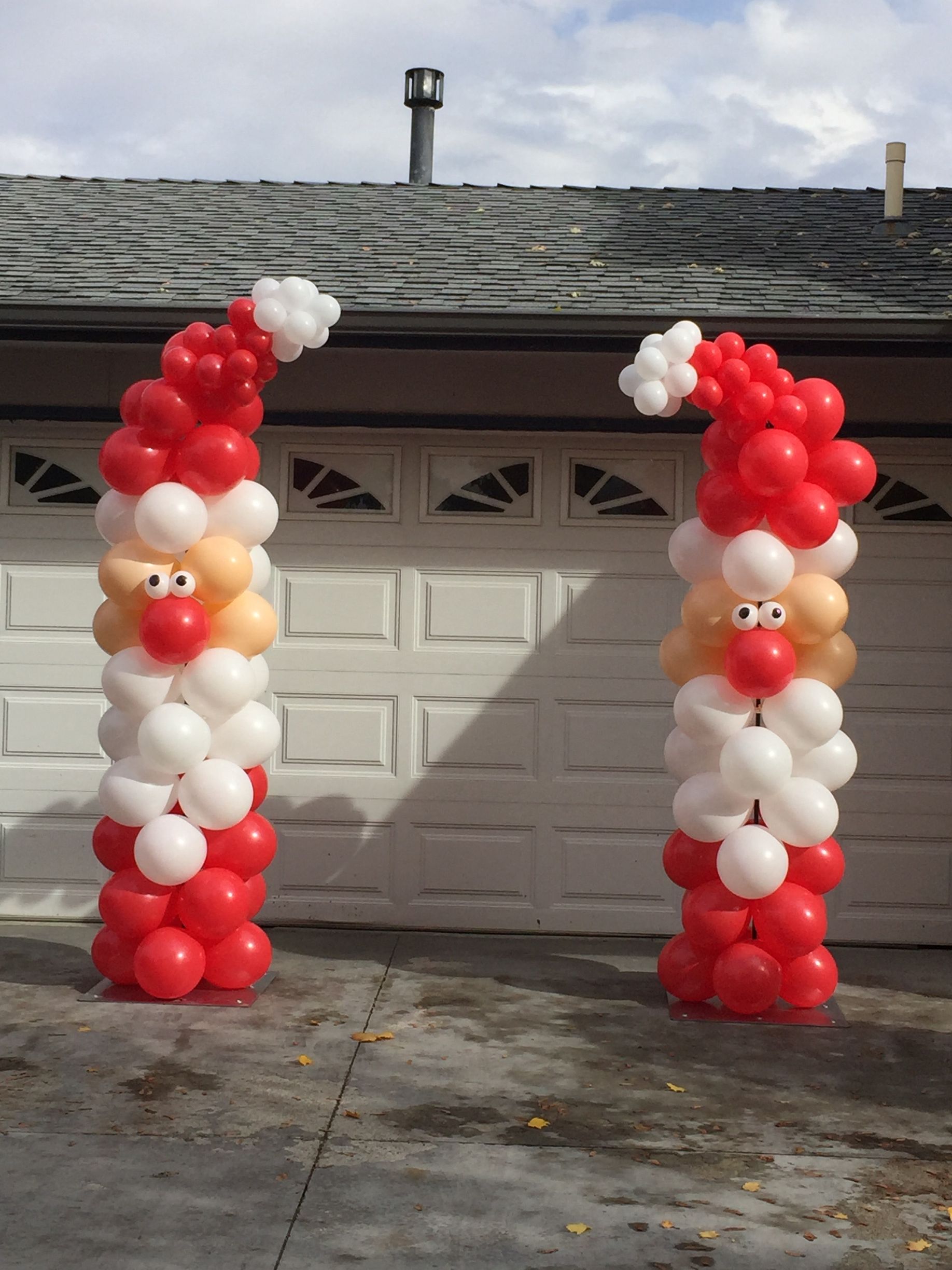 Two santa clauses made out of balloons in front of a garage door