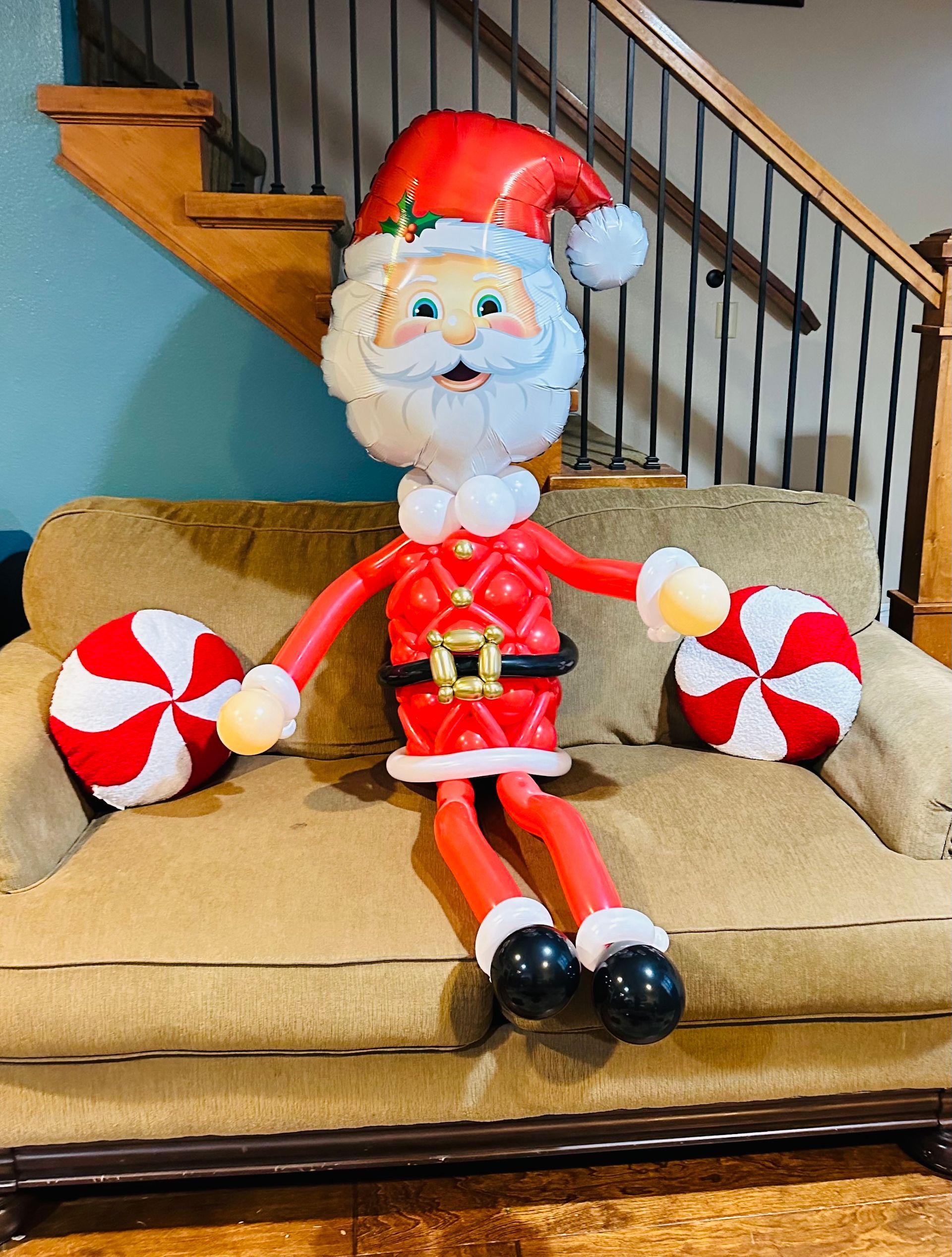 A santa claus balloon is sitting on a couch holding candy canes.