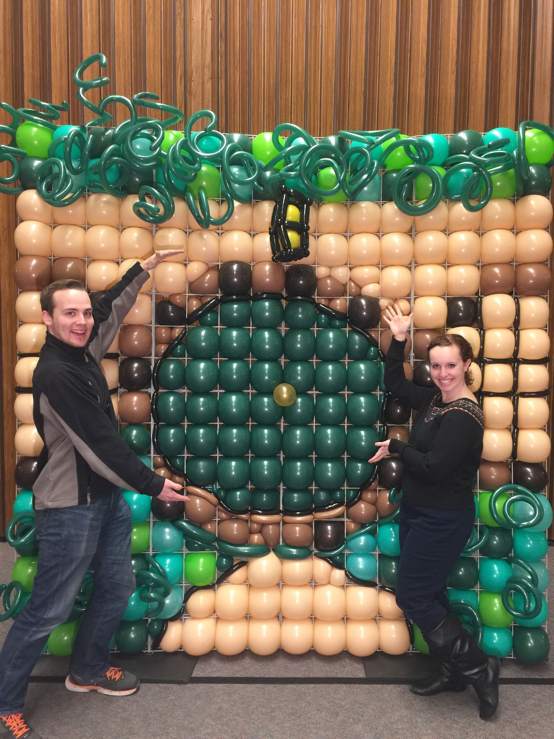 A man and a woman are standing in front of a wall made of balloons.