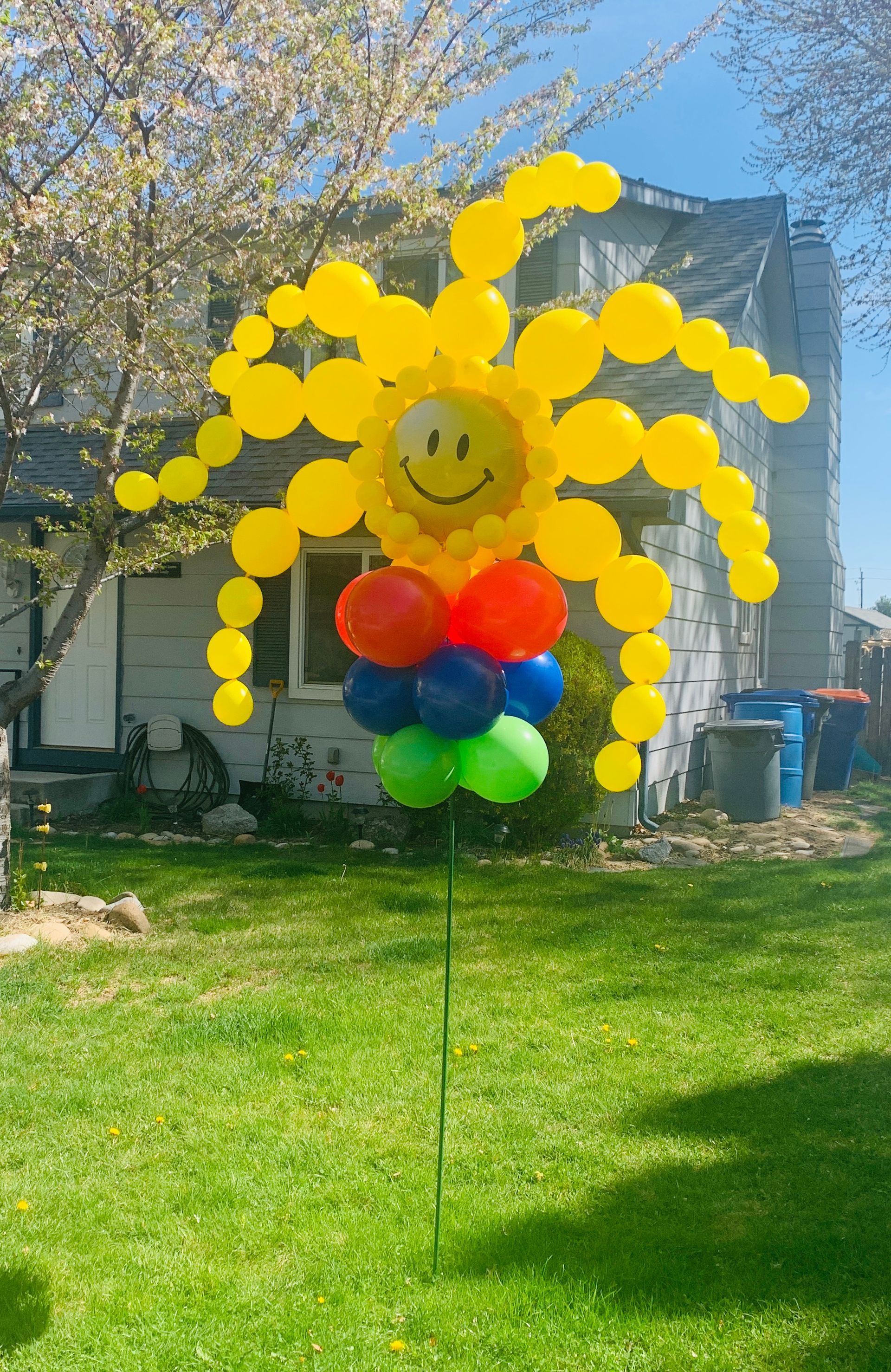 A sun made out of balloons is sitting on top of a lawn in front of a house.
