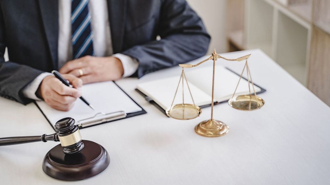 Lawyer in suit writing, scale of justice, and gavel on a desk.