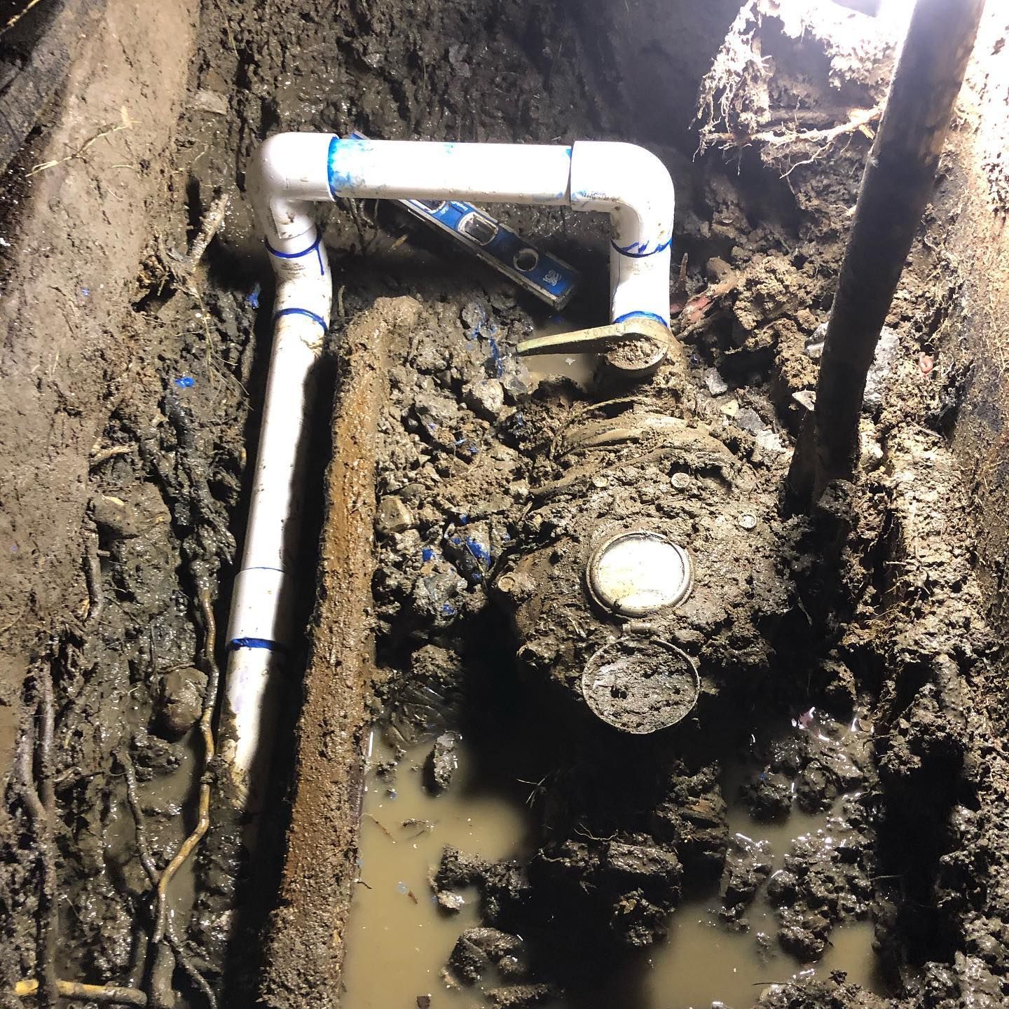 A water meter is sitting in the mud next to a pipe
