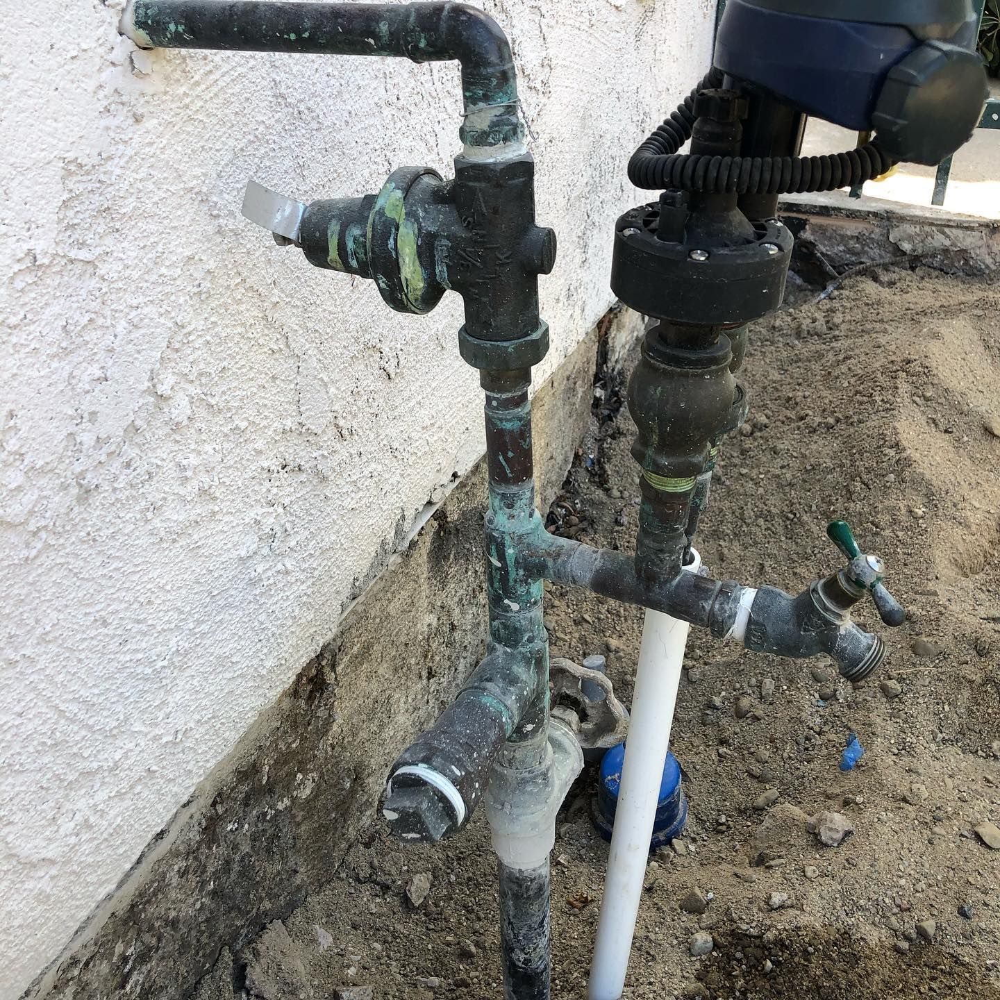 A water pipe is sitting in the dirt next to a wall.