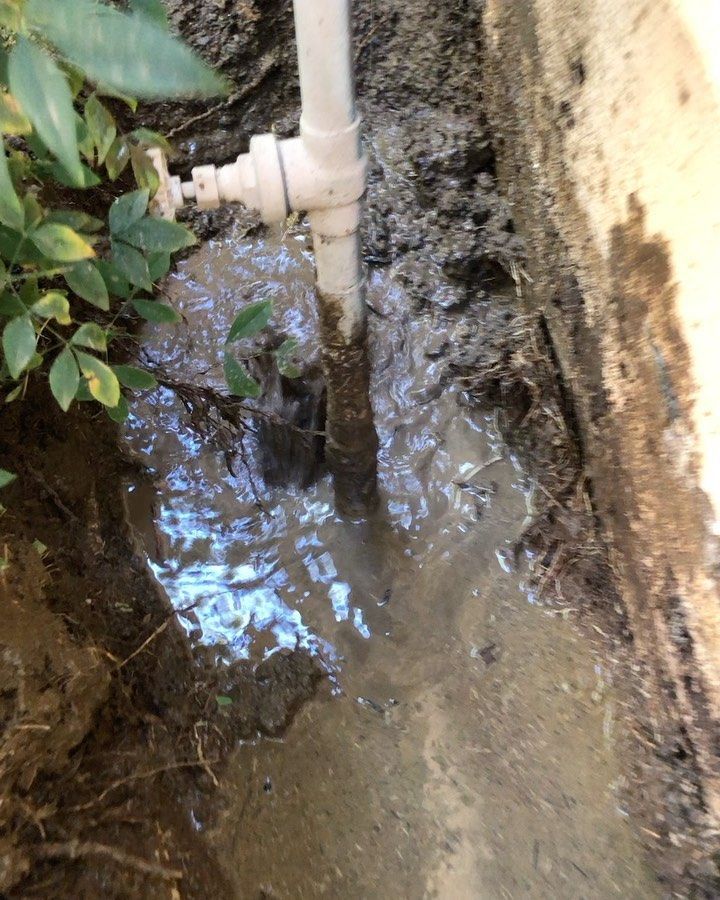 A white pipe is sitting in the mud next to a wall.