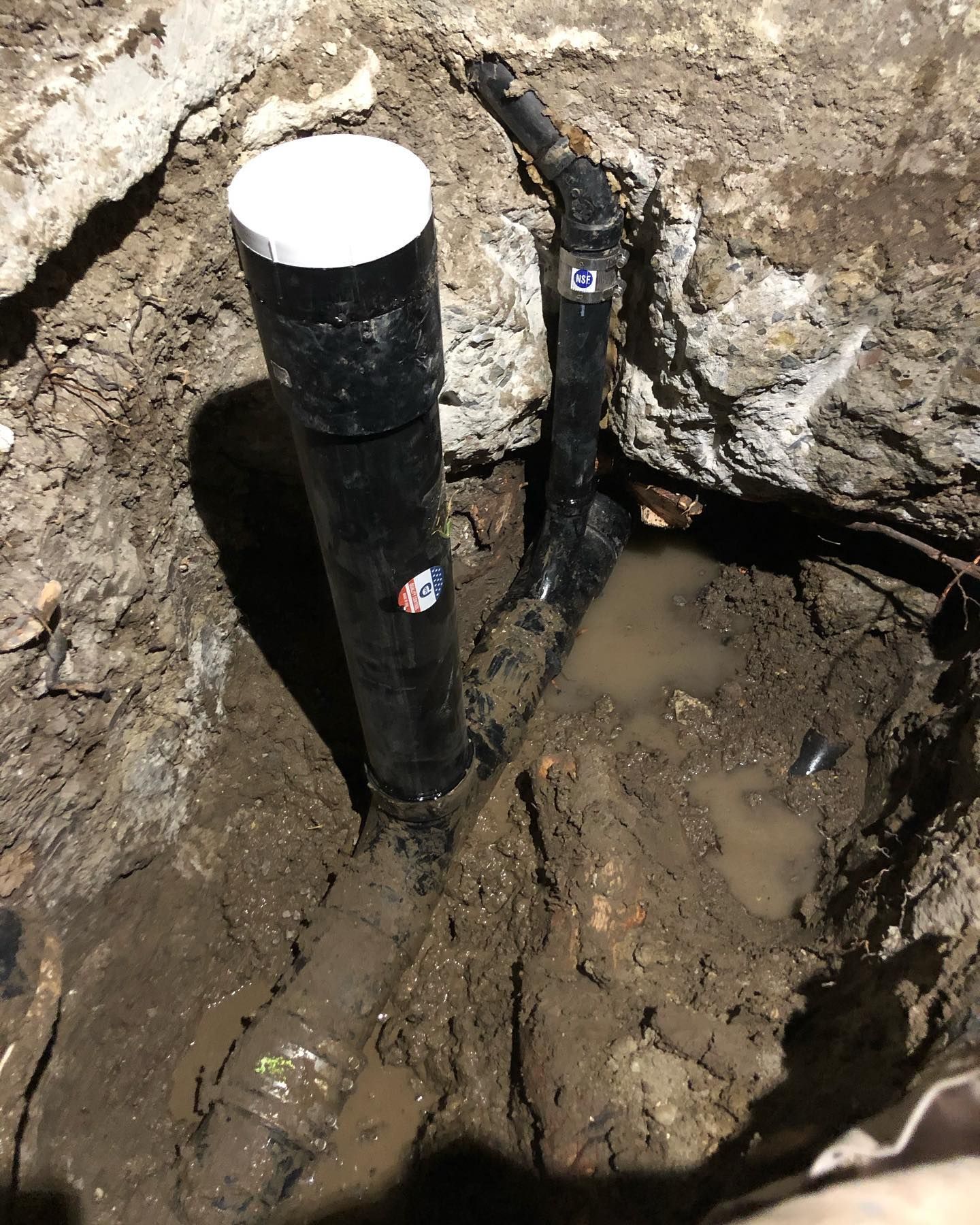 A black pipe is sitting in the dirt next to a rock.