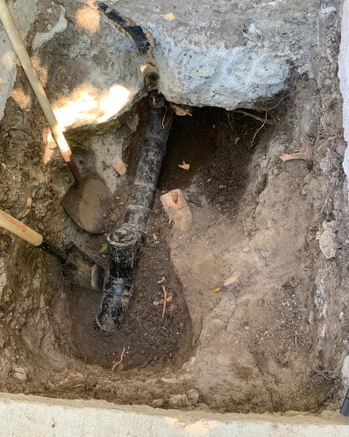 A pipe is laying in the dirt next to a rock.
