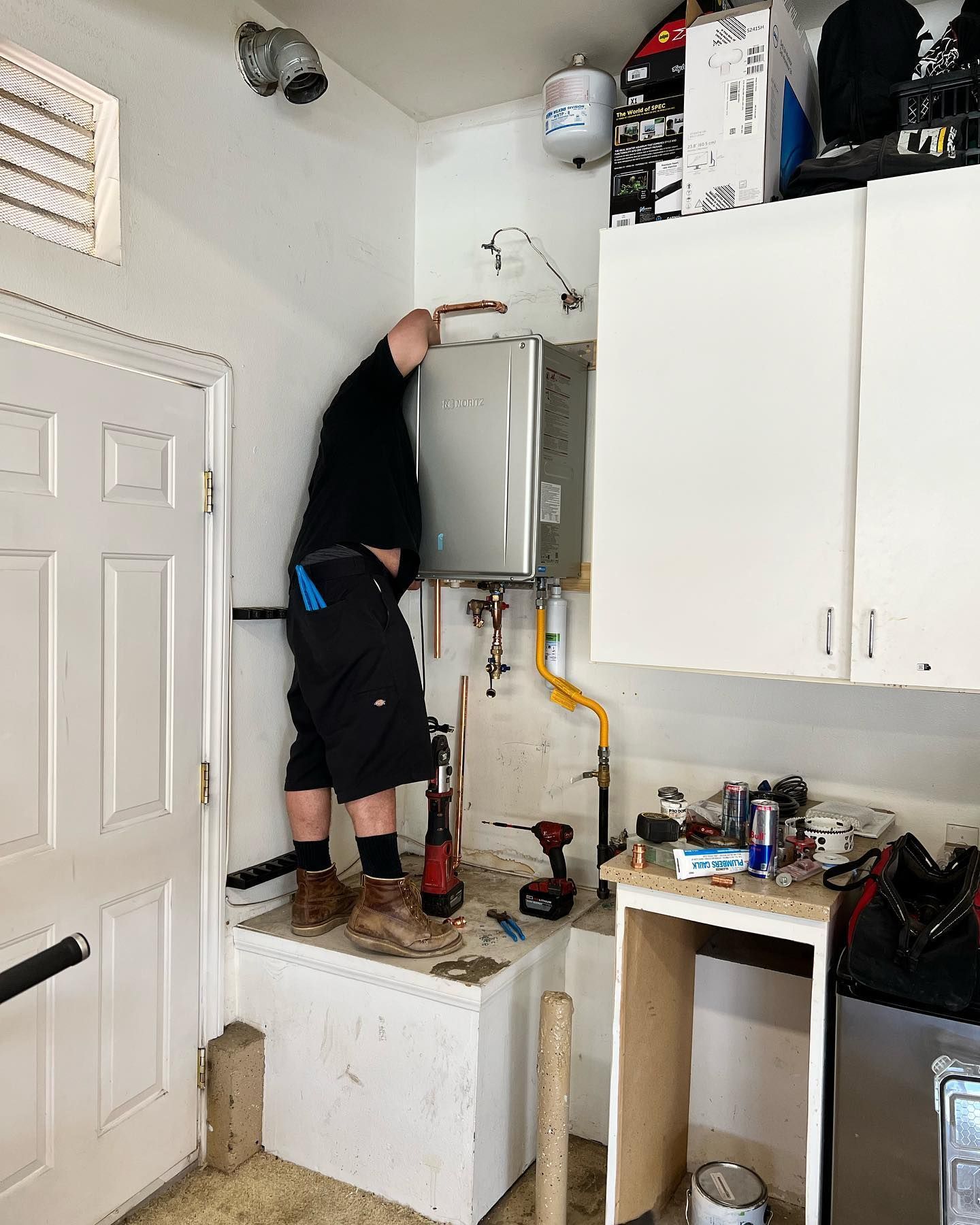 A man is working on a water heater in a garage.