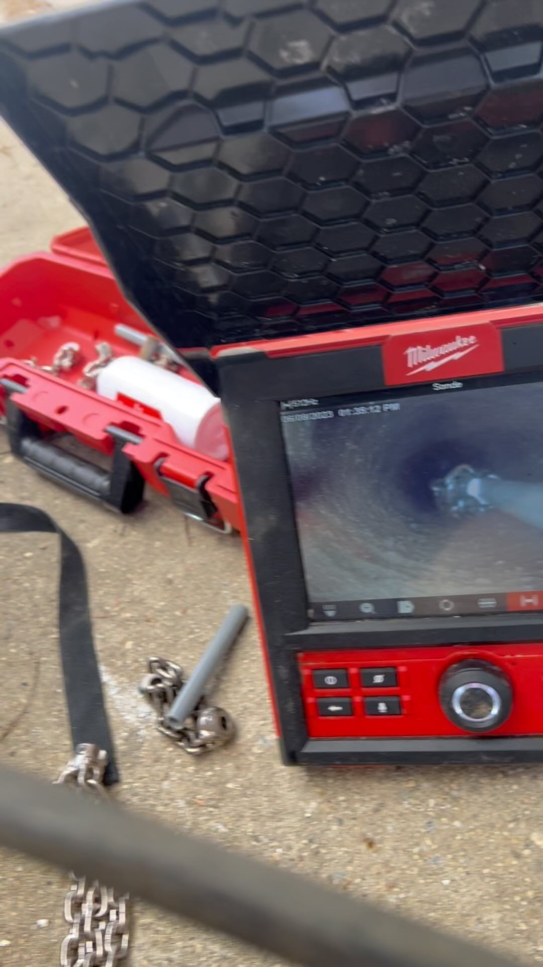 A red and black device is sitting on the ground next to a hose.