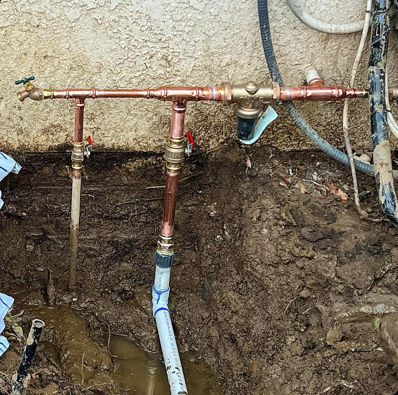 A copper pipe is sitting in the dirt next to a wall.