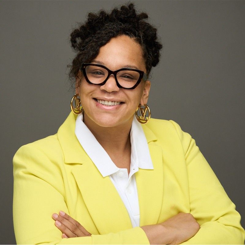 A woman wearing glasses and a yellow jacket smiles for the camera