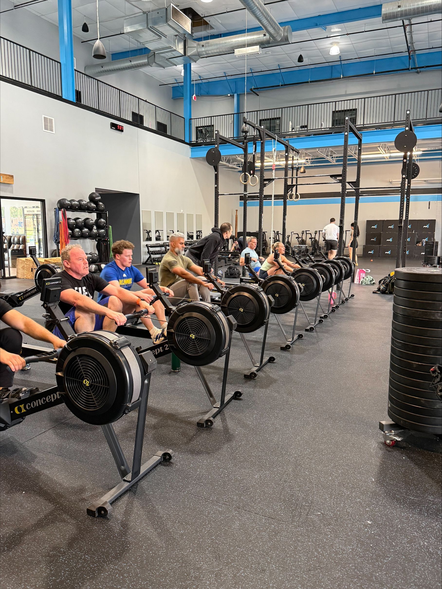 Group of people posing in a gym, standing on a black floor with blue pillars and workout rig behind them.