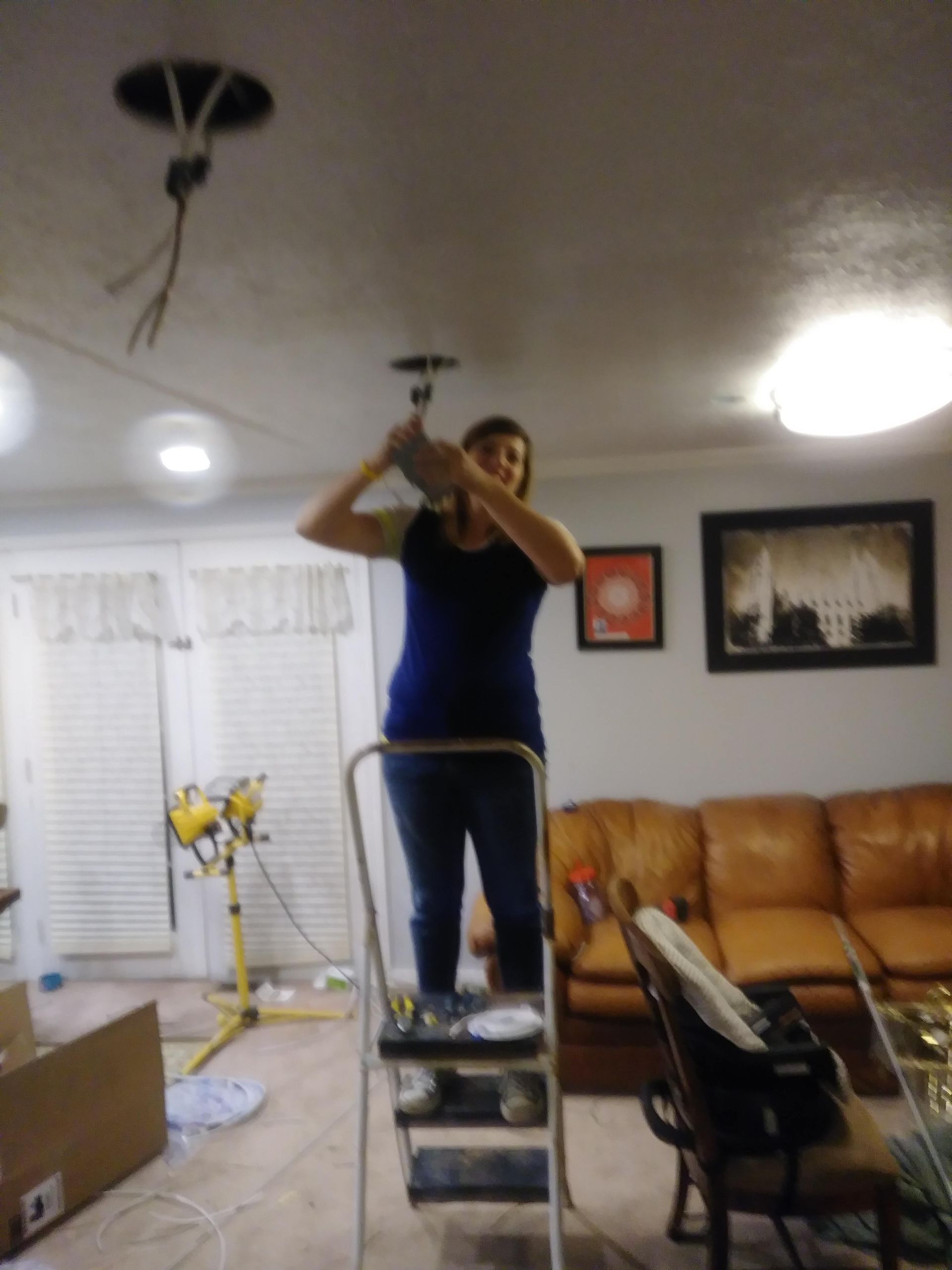 A woman is standing on a ladder in a living room fixing a light fixture