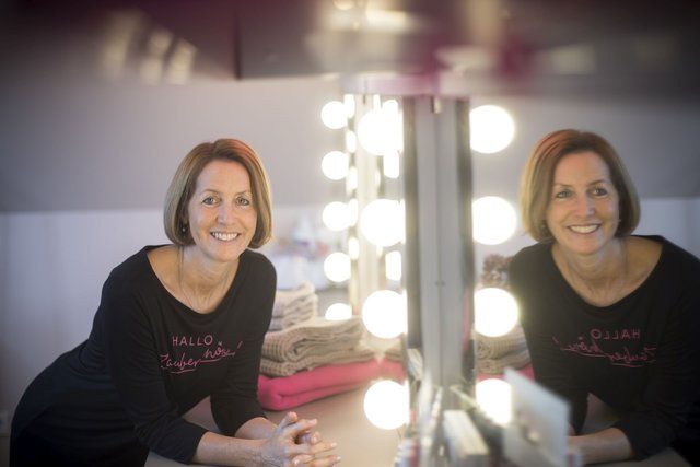 Zwei Frauen sitzen vor einem Spiegel und lächeln.