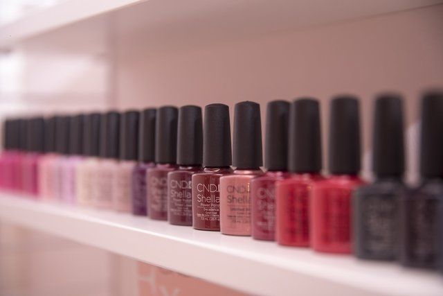 Mehrere Flaschen Nagellack stehen aufgereiht auf einem Regal