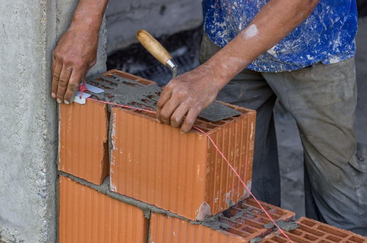 “Worker aligning red masonry blocks with a level and guide string during a masonry service in Missouri City, TX”