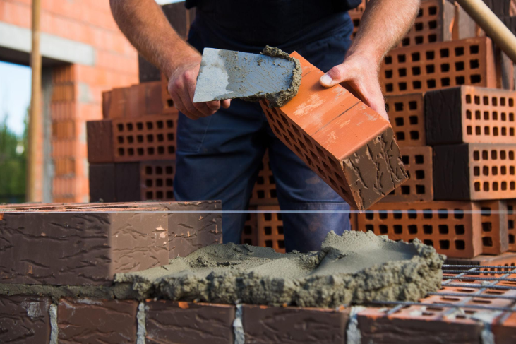 “Close-up of a worker spreading mortar onto a red brick before placement during a masonry service in Missouri City, TX”