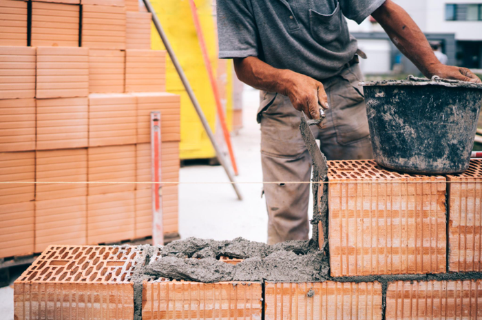 “Worker preparing mortar beside stacked red masonry blocks at a construction site during a masonry service in Missouri City, TX”