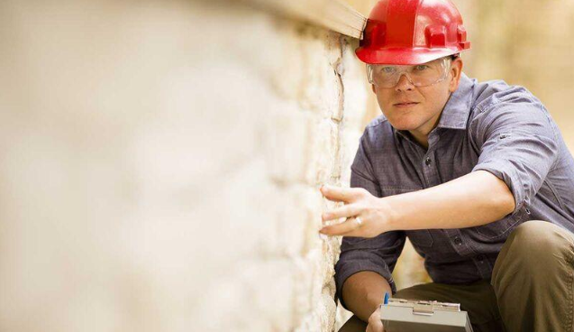 “Mason in a red hard hat inspecting a stone wall for repair and restoration during a masonry service in Missouri City, TX”