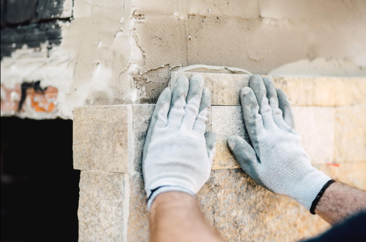 “Worker carefully setting a light stone block into place by hand during a masonry service in Missouri City, TX”