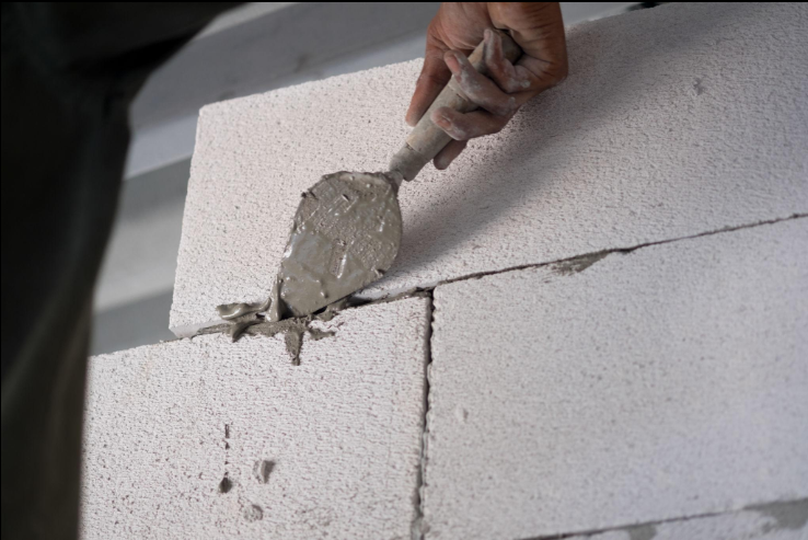 “Worker using a trowel to apply mortar between light stone blocks during a masonry service in Missouri City, TX”